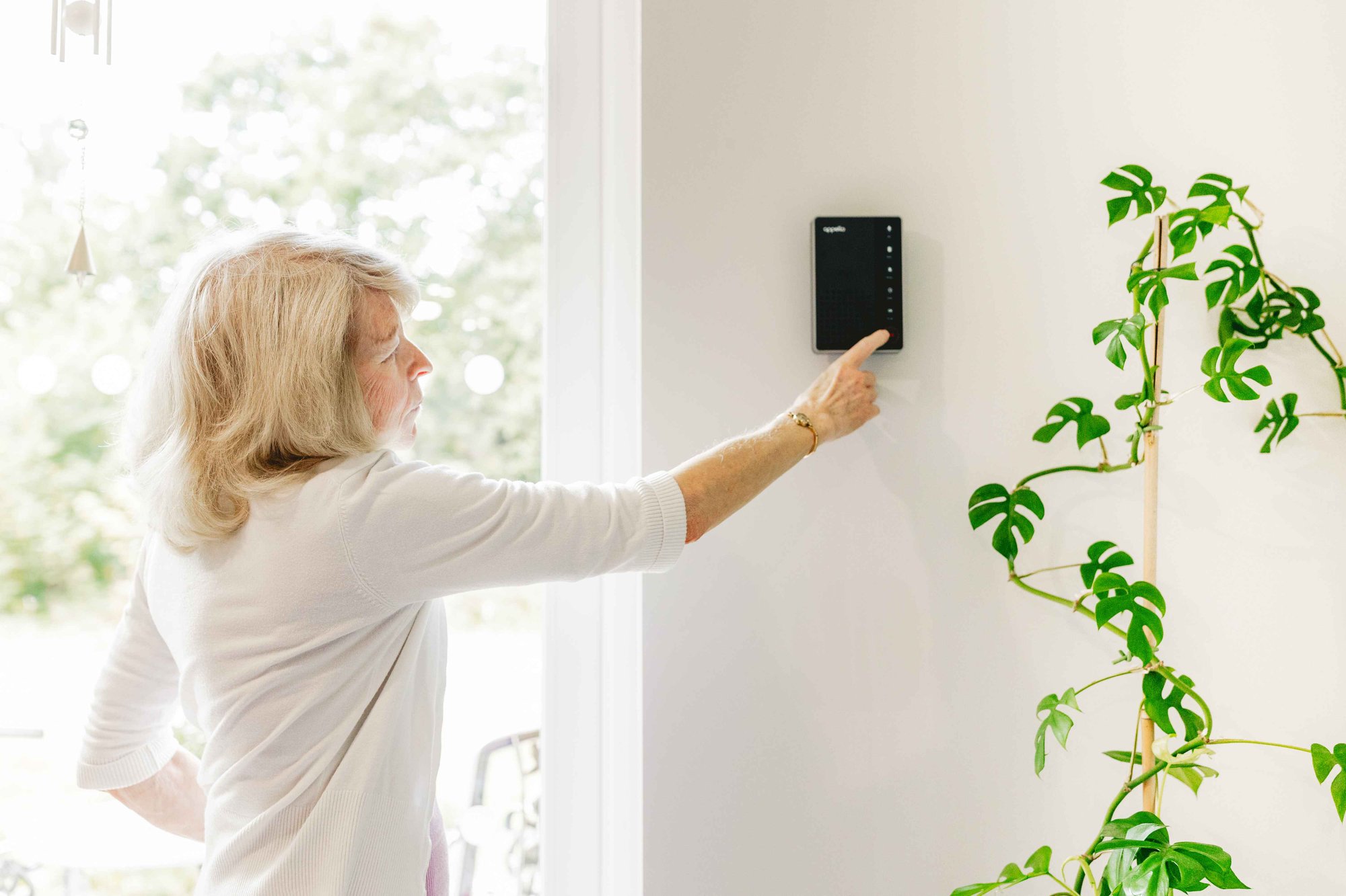 Warden call system on the wall with elderly woman pressing the button.