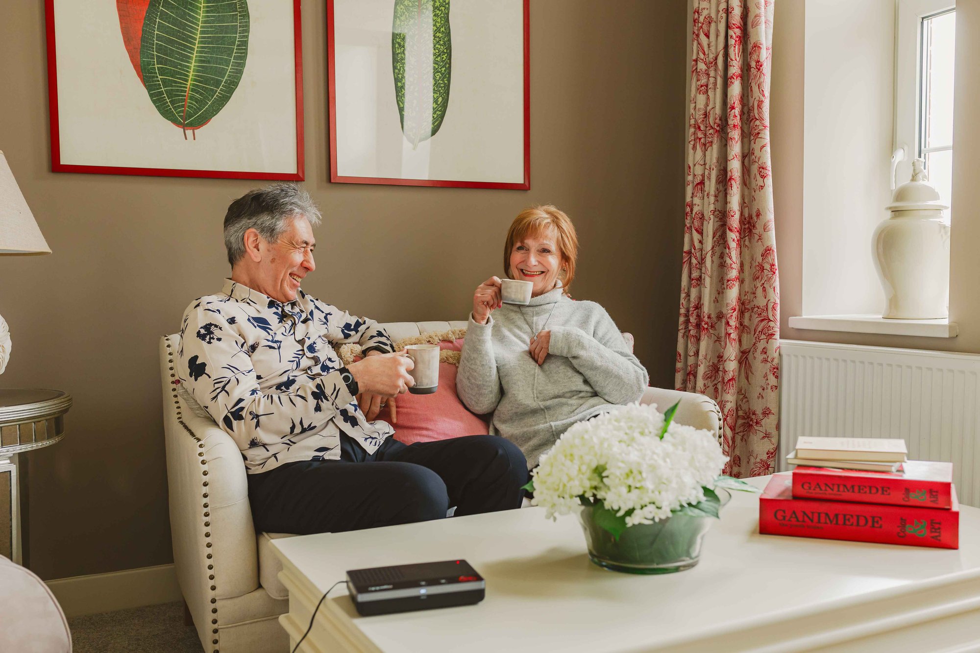 Elderly couple, drinking a cup of tea with dispersed alarm on the table.