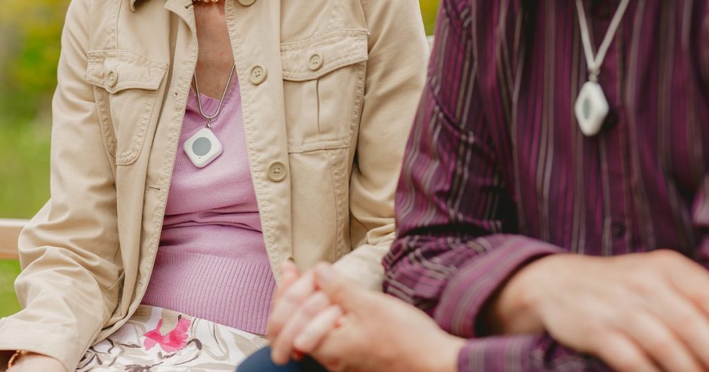 Two elderly people holding hands with pendant around their necks